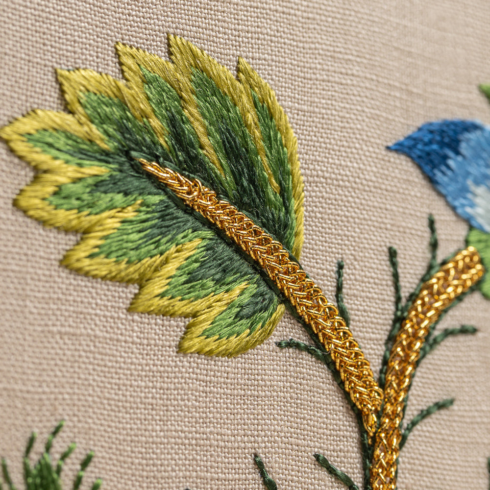 Embroidered floral design with green leaves and a blue flower on beige fabric.