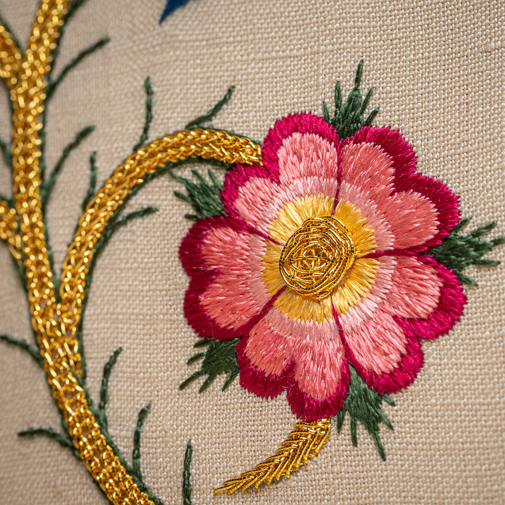 Close-up of an embroidered pink flower with a yellow center on beige fabric.