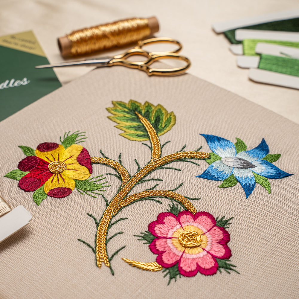 Embroidery hoop with floral design on fabric, surrounded by embroidery supplies.
