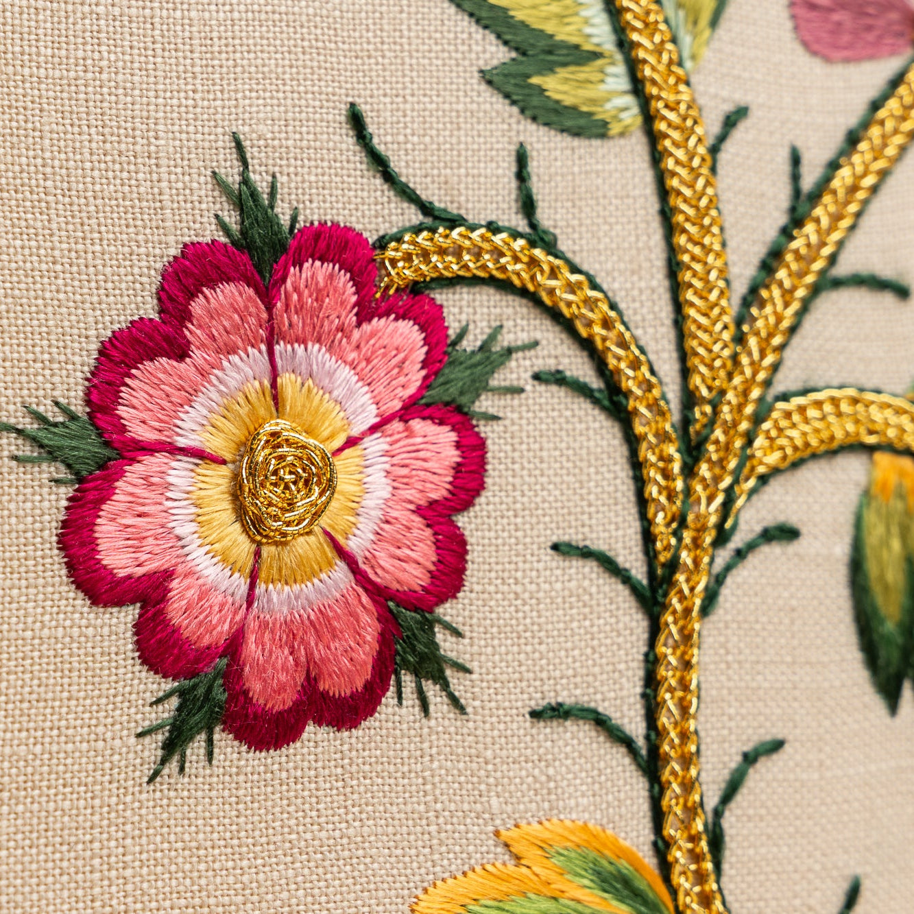 Close-up of an embroidered floral design on fabric with a pink flower and gold branch.