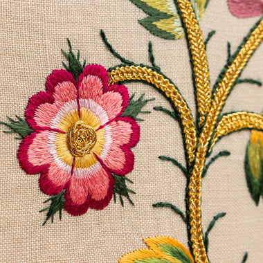 Close-up of an embroidered floral design on fabric with a pink flower and gold branch.